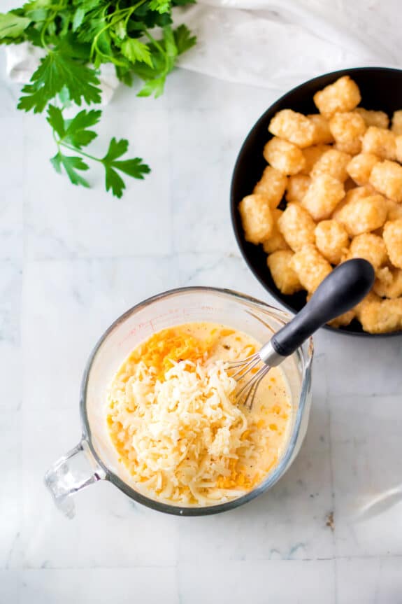 A glass measuring cup with a whisk. Eggs, milk, half-and-half, and cajun seasoning for Slow Cooker Tator Tot Breakfast Casserole recipe.