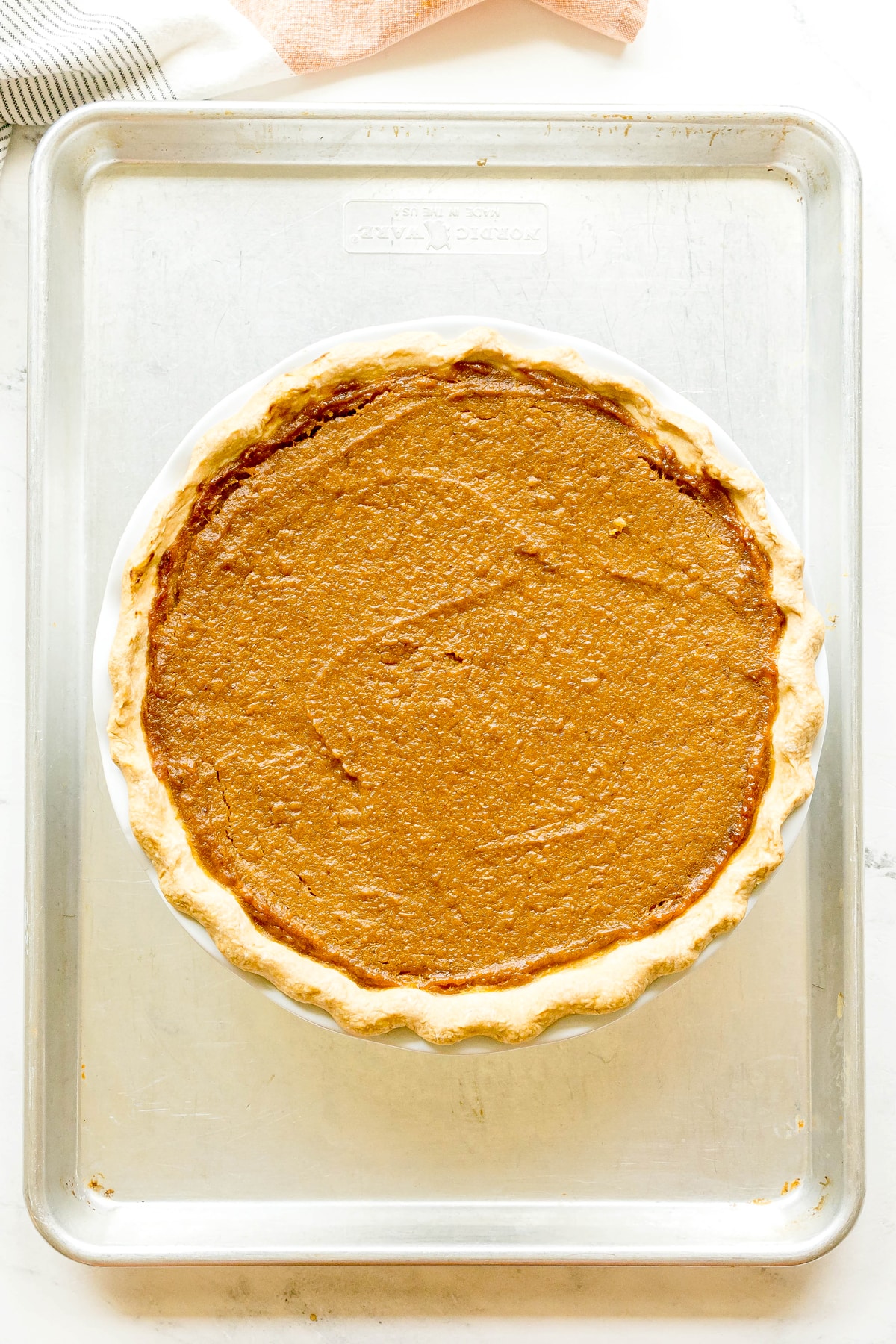 A baked Sweet Potato Pie with a golden crust sits on a metal baking sheet, viewed from above.