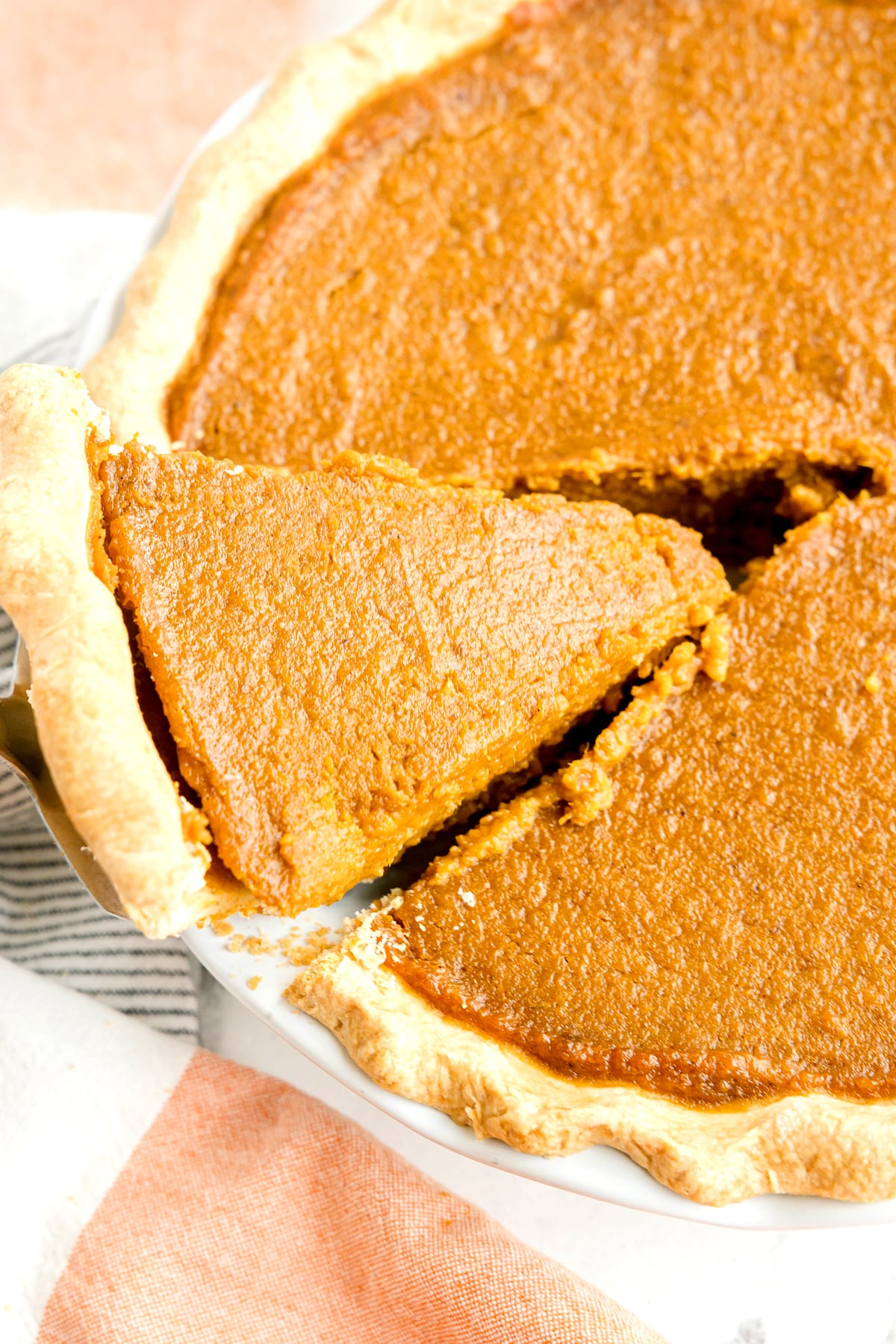 A close-up of a Sweet Potato Pie with one slice being lifted from the dish, showing the smooth filling and golden crust.