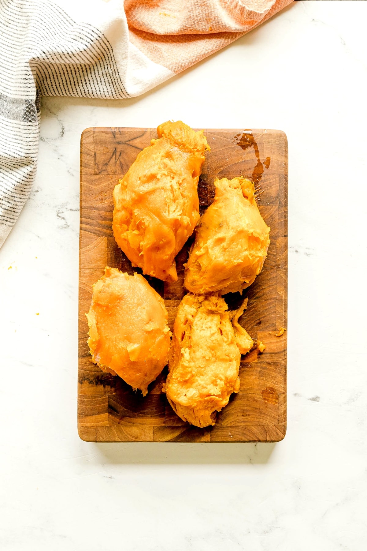 Four pieces of peeled sweet potato on a wooden cutting board, with two striped kitchen towels partially visible in the background for Sweet Potato Pie recipe.