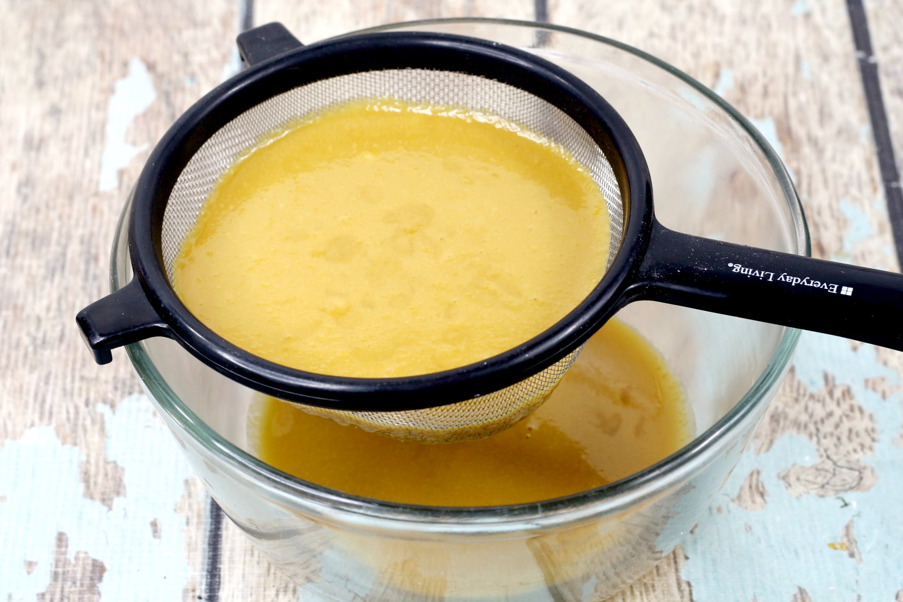 A metal strainer with yellow liquid is placed over a glass bowl, with some liquid collected in the bowl below, this is for German Chocolate Brownies recipe.