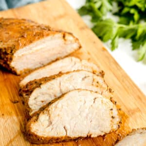 Air Fryer Pork Tenderloin slices on wooden board with parsley on the side