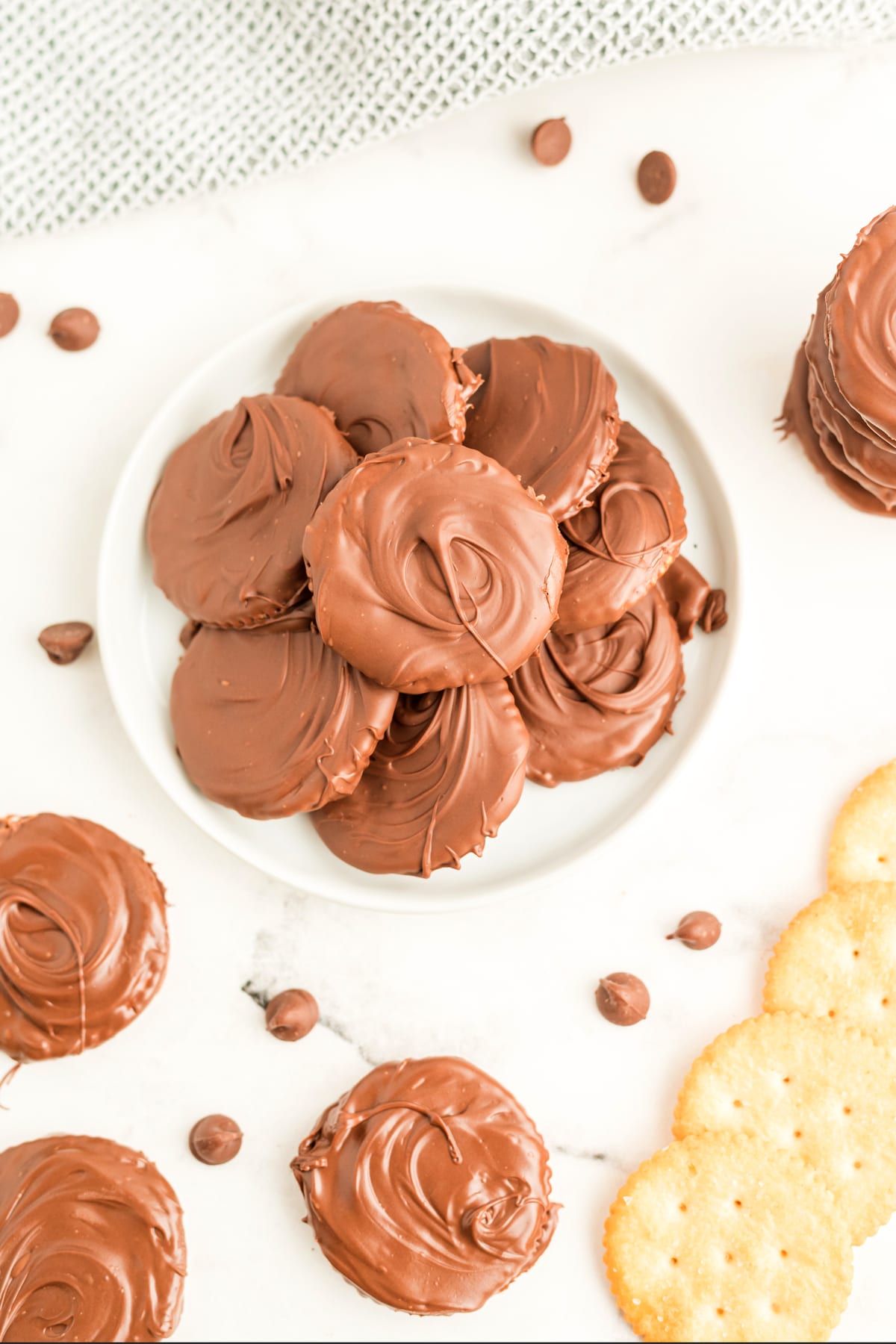 A plate of Ritz Cracker Thin Mints sits on a white surface, surrounded by more cookies, chocolate chips, and plain round crackers.