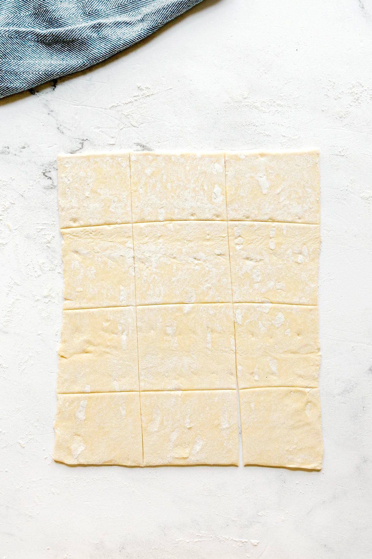 First step in preparing Cranberry Brie Bites is to use a sheet of dough and cut into 24 slices and is lightly floured, a piece of blue cloth visible in the top corner.