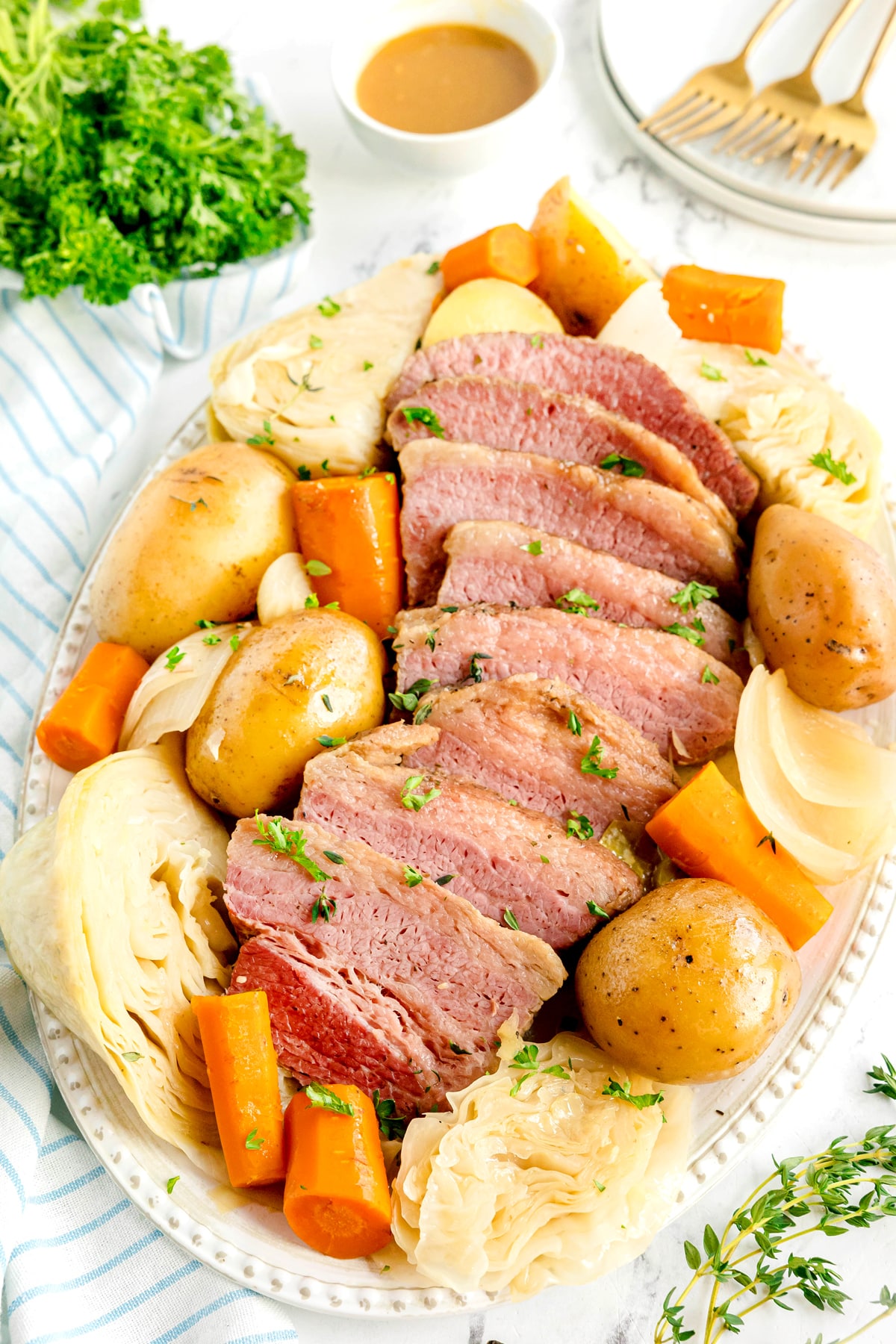 Oval platter of Crockpot Corned Beef and Cabbage, garnished with parsley; a bowl of sauce and some utensils are in the background.