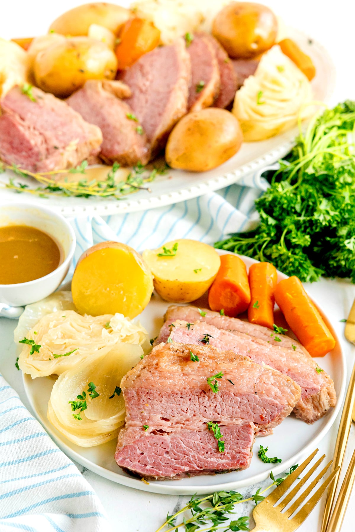 Crockpot Corned Beef and Cabbage consisting of slices of corned beef with potatoes, carrots, cabbage, and onions on a plate, garnished with parsley, with mustard sauce on the side.