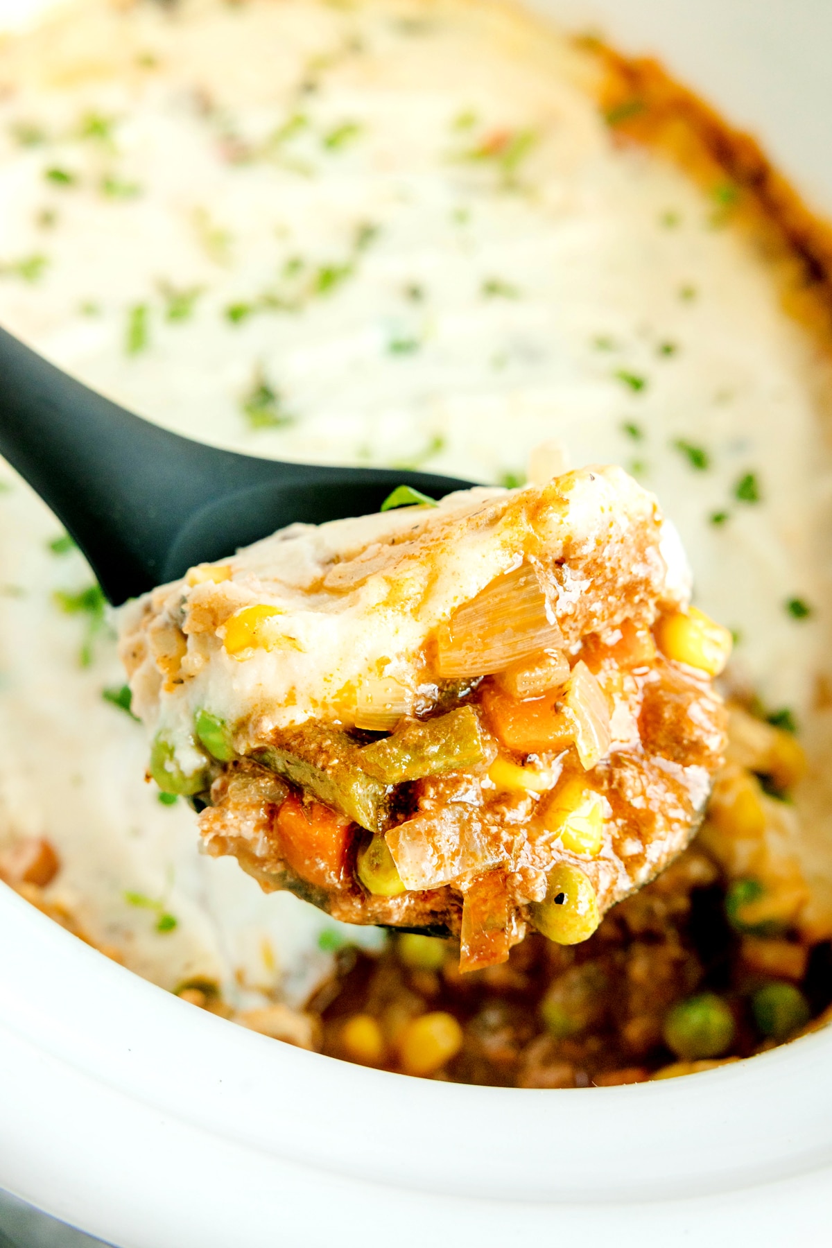 A close-up of a spoonful of Crockpot Shepherd's Pie with visible mixed vegetables, mashed potatoes, and chopped herbs on top.