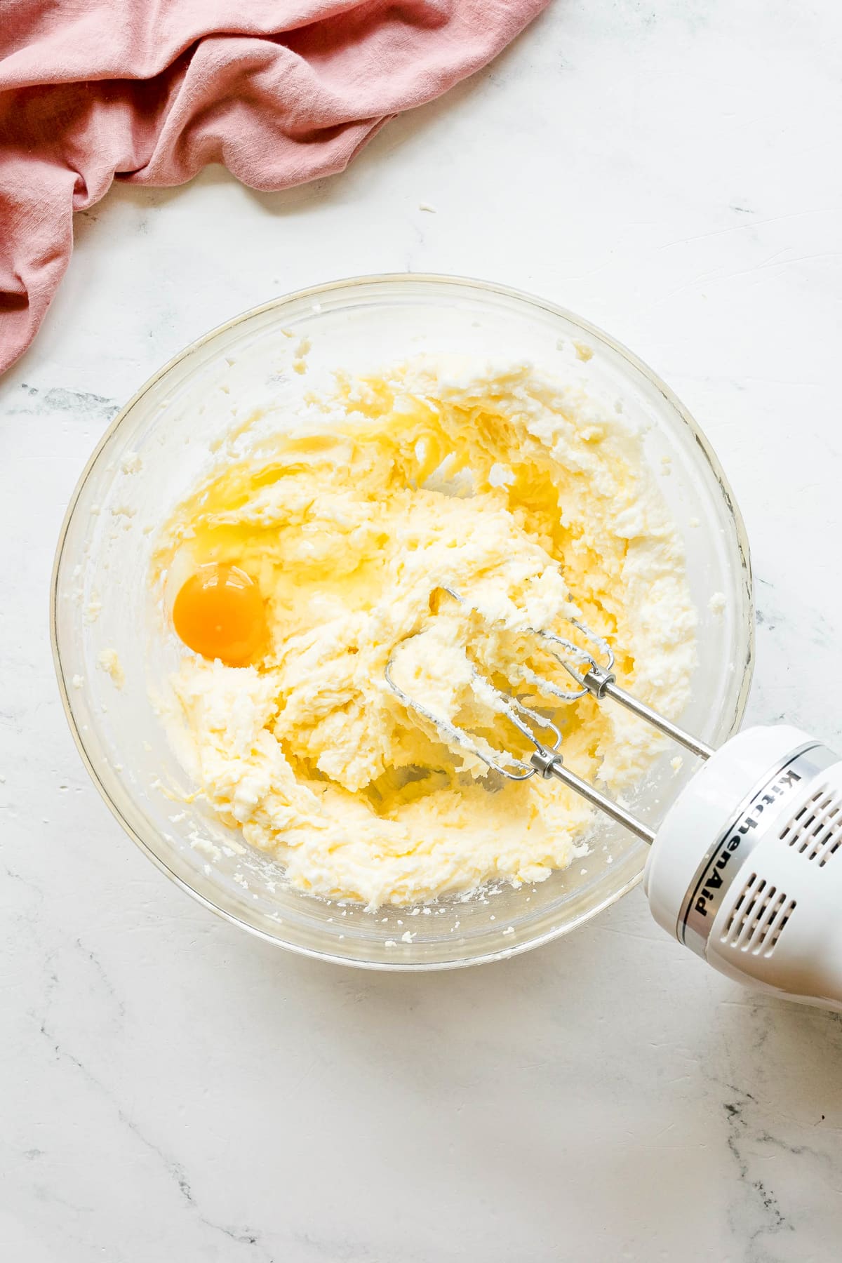Next step in preparing Paula Deen Pound Cake is to add egg to creamed butter, suga, while being mixed with a handheld electric mixer on a white surface.