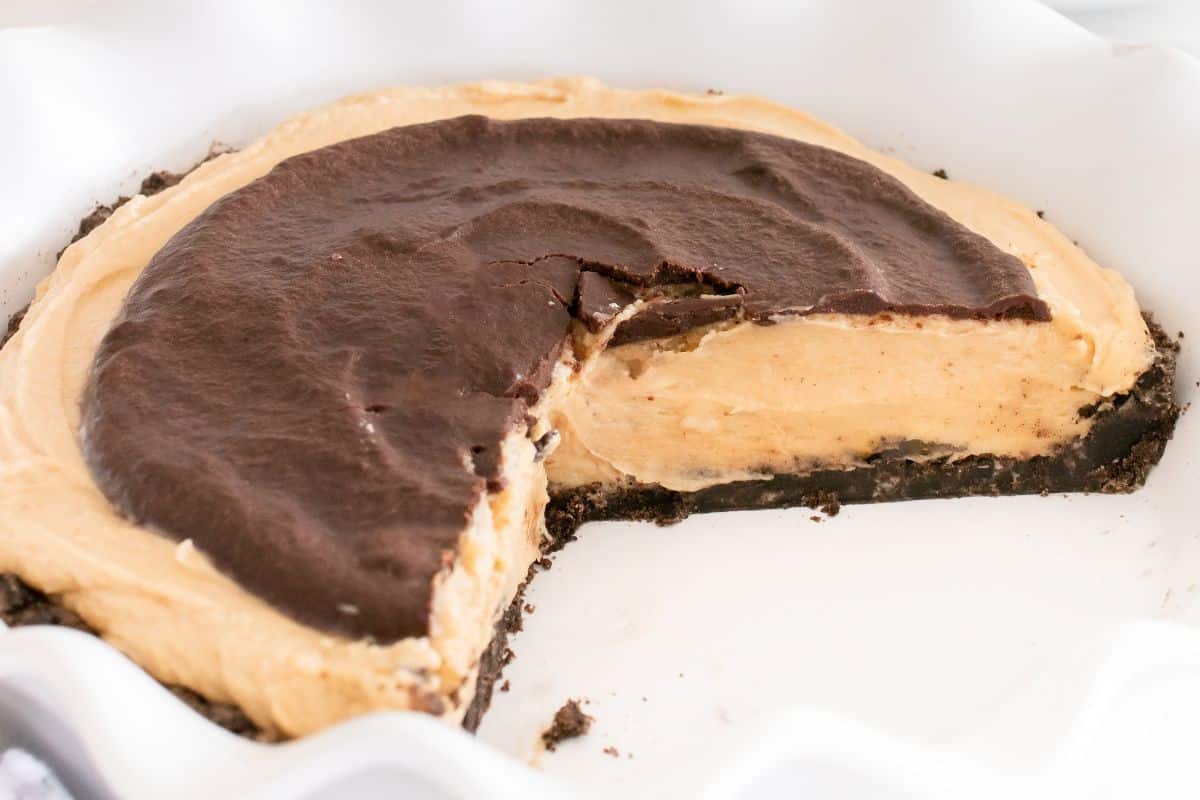 A Buckeye pie with a chocolate topping and chocolate crust in a white pie dish, with a slice removed.