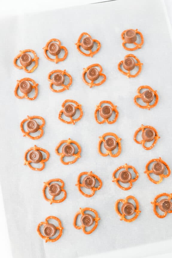 Rows of pretzels topped with chocolate candies are arranged on a sheet of parchment paper.
