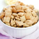 A white bowl filled with Churro Muddy Buddies recipe sits on a light pink cloth.