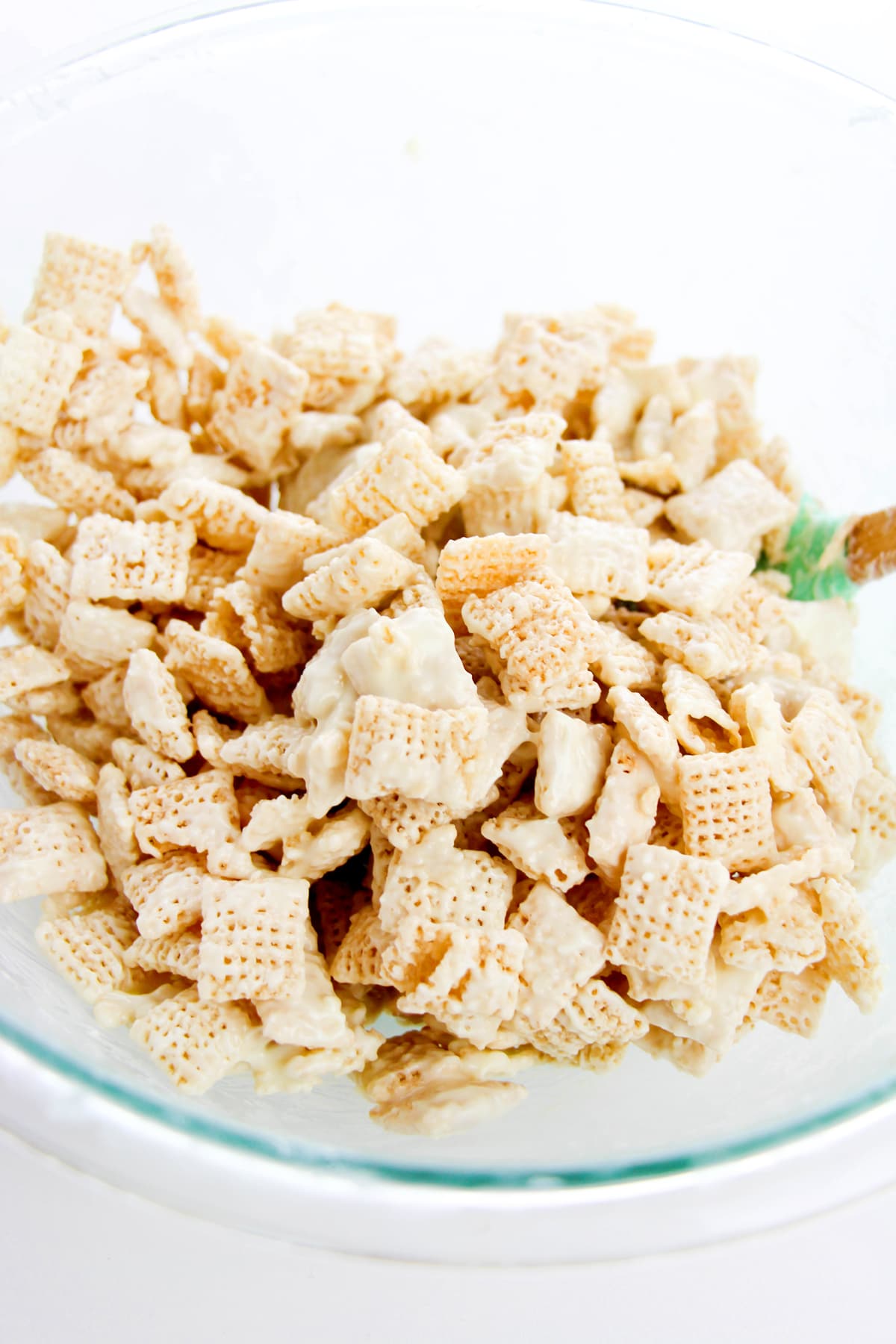 A glass bowl filled with Chex cereal pieces coated in a white, creamy mixture or Churro Muddy Buddies recipe.