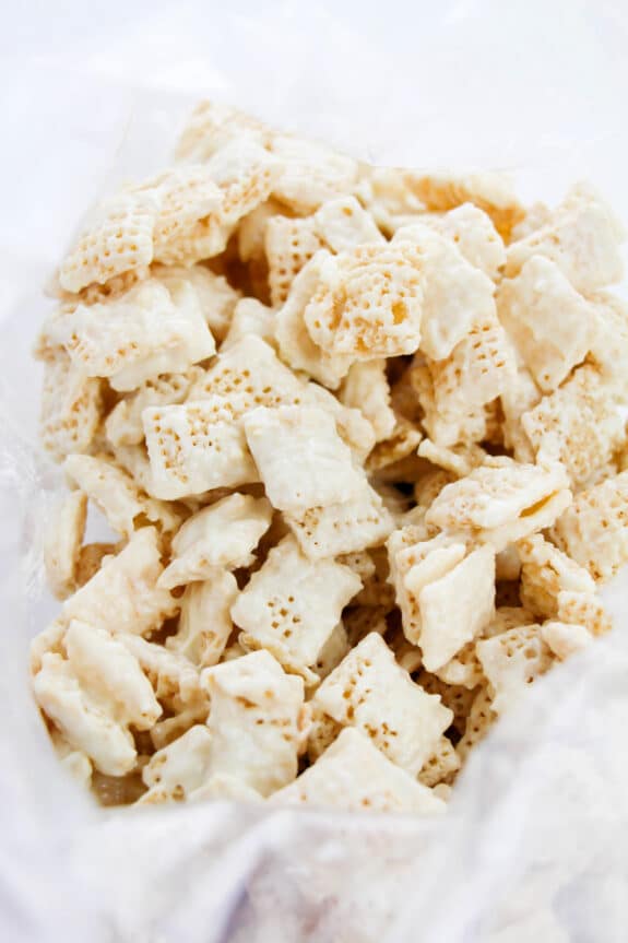 White chocolate-coated Chex cereal pieces in a clear plastic bag. This is one step in preparing Churro Muddy Buddies recipe.