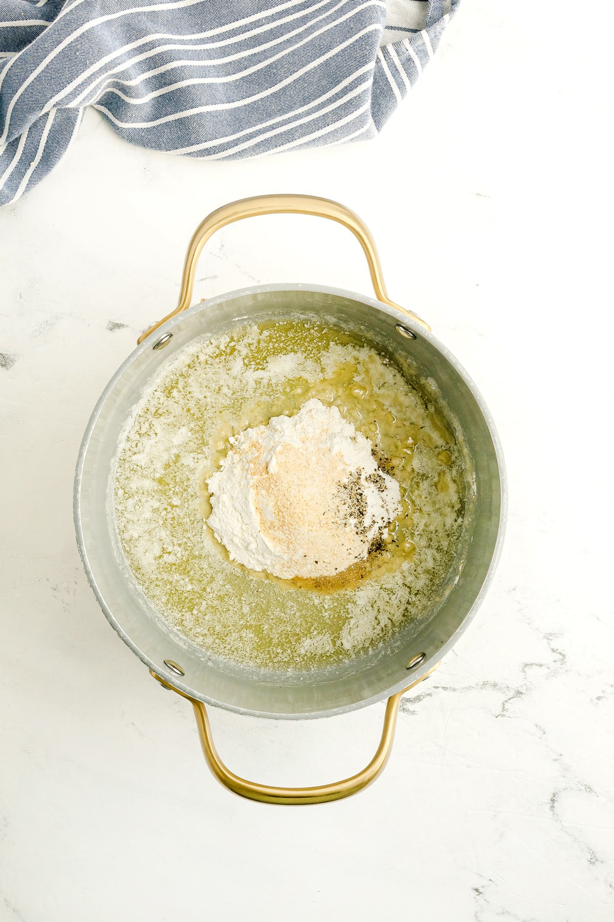A metal pot containing melted butter topped with a mound of flour and seasonings, with a striped kitchen towel nearby. This is the first step in preparing Chicken Gravy Recipe.