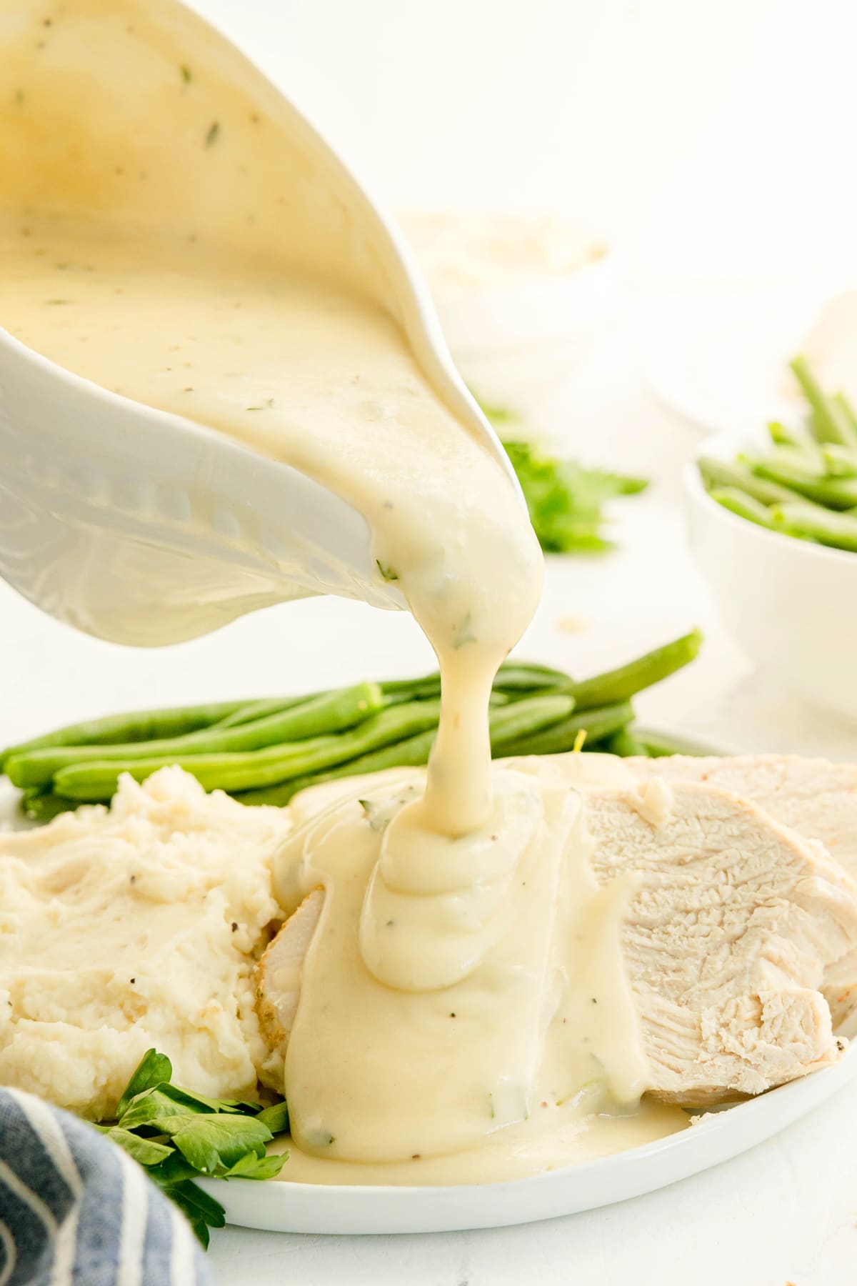 Chicken Gravy being poured from a boat over sliced turkey, mashed potatoes, and green beans.