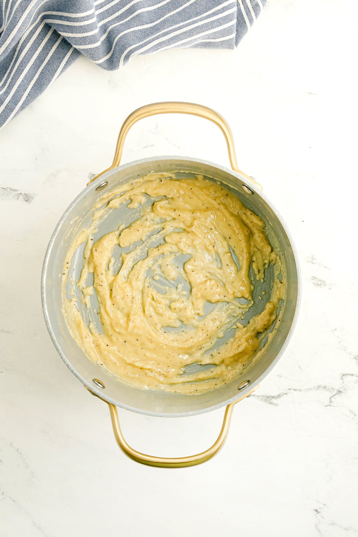 A pan containing melted butter added with flour, garlic powder and onion powder in a pan, with visible black pepper, with a striped kitchen towel nearby.