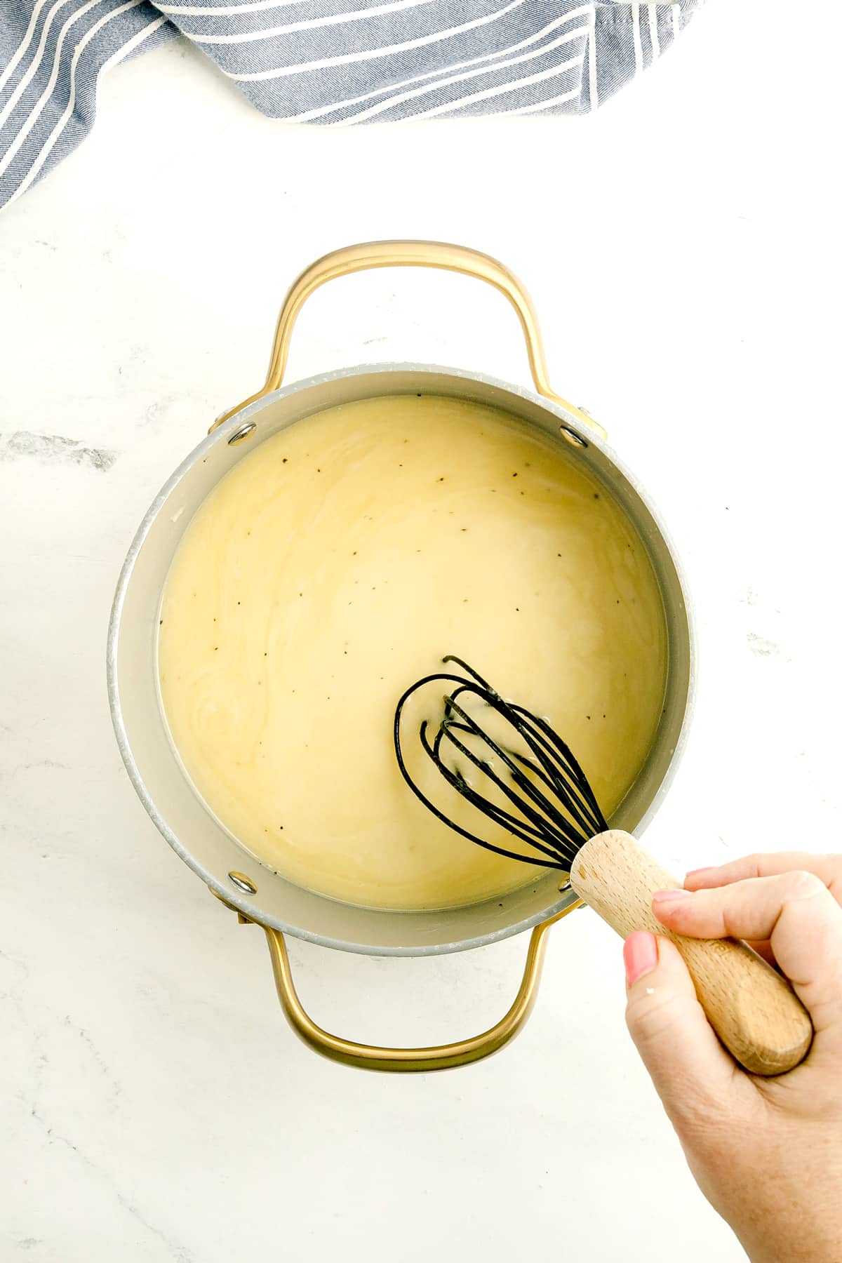 One of the steps in preparing Chicken Gravy Recipeis to add chicken broth to the mixture and whisk it to stir a pale yellow sauce in a metal pot with gold handles.