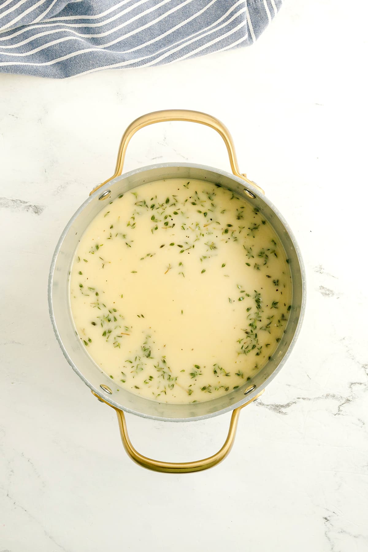 Chicken Gravy with fresh herbs in a metal pot with gold handles.