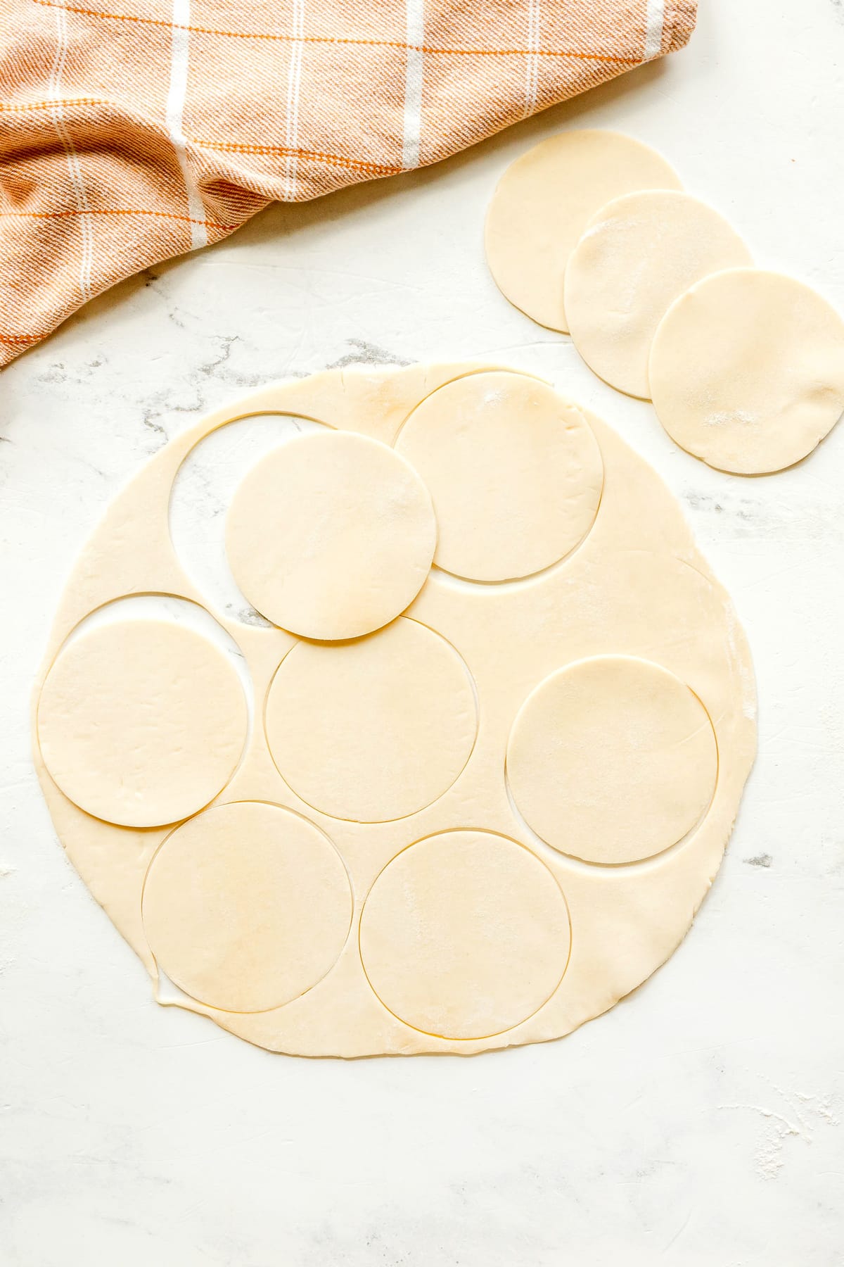 Rolled out dough for Mini Pumpkin Pies on a white surface and cut out several circles from it.