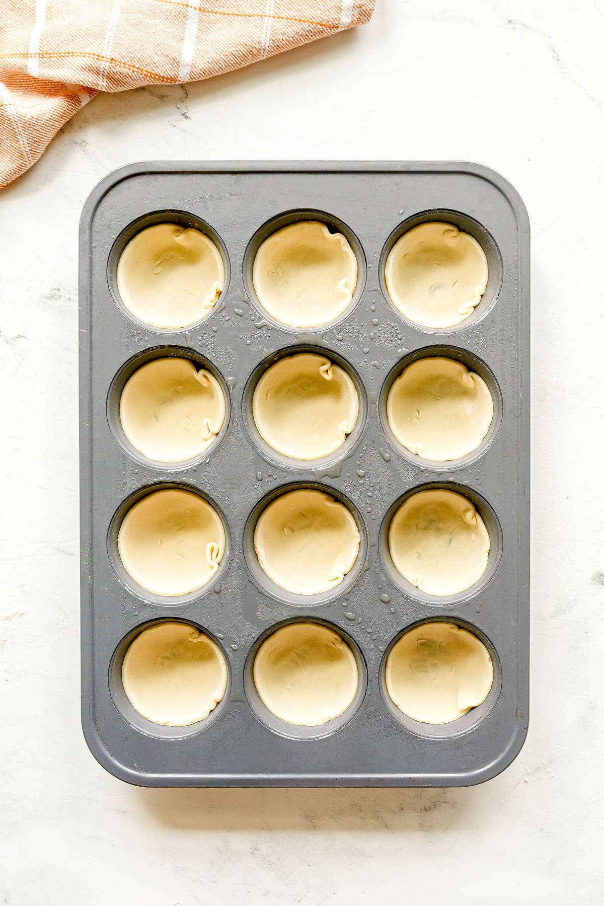 Another step in preparing Mini Pumpkin Pies is to press 12 pie crusts into a muffin tin.