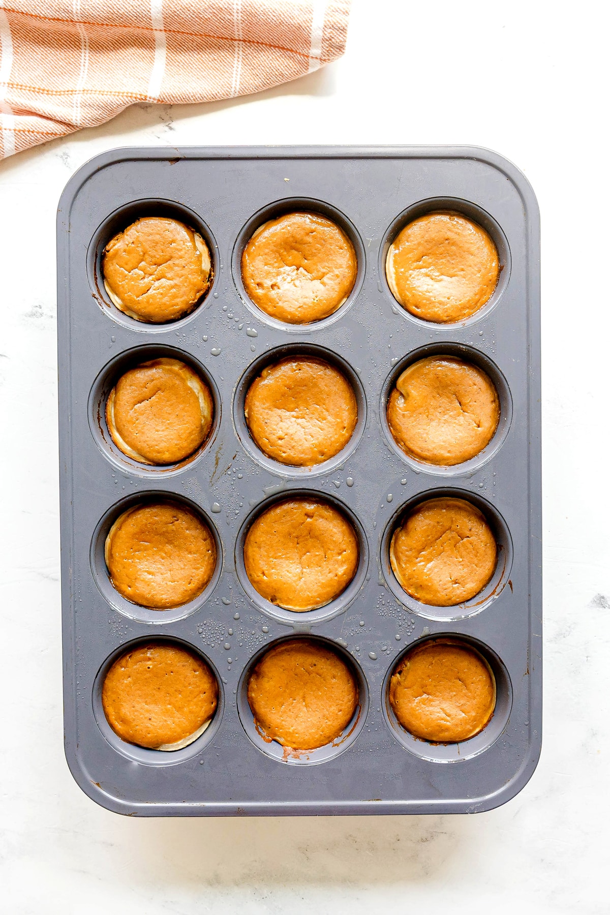 Twelve baked Mini Pumpkin Pies in a metal muffin tin.