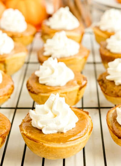 A grid of Mini Pumpkin Pies topped with whipped cream on a wire cooling rack.