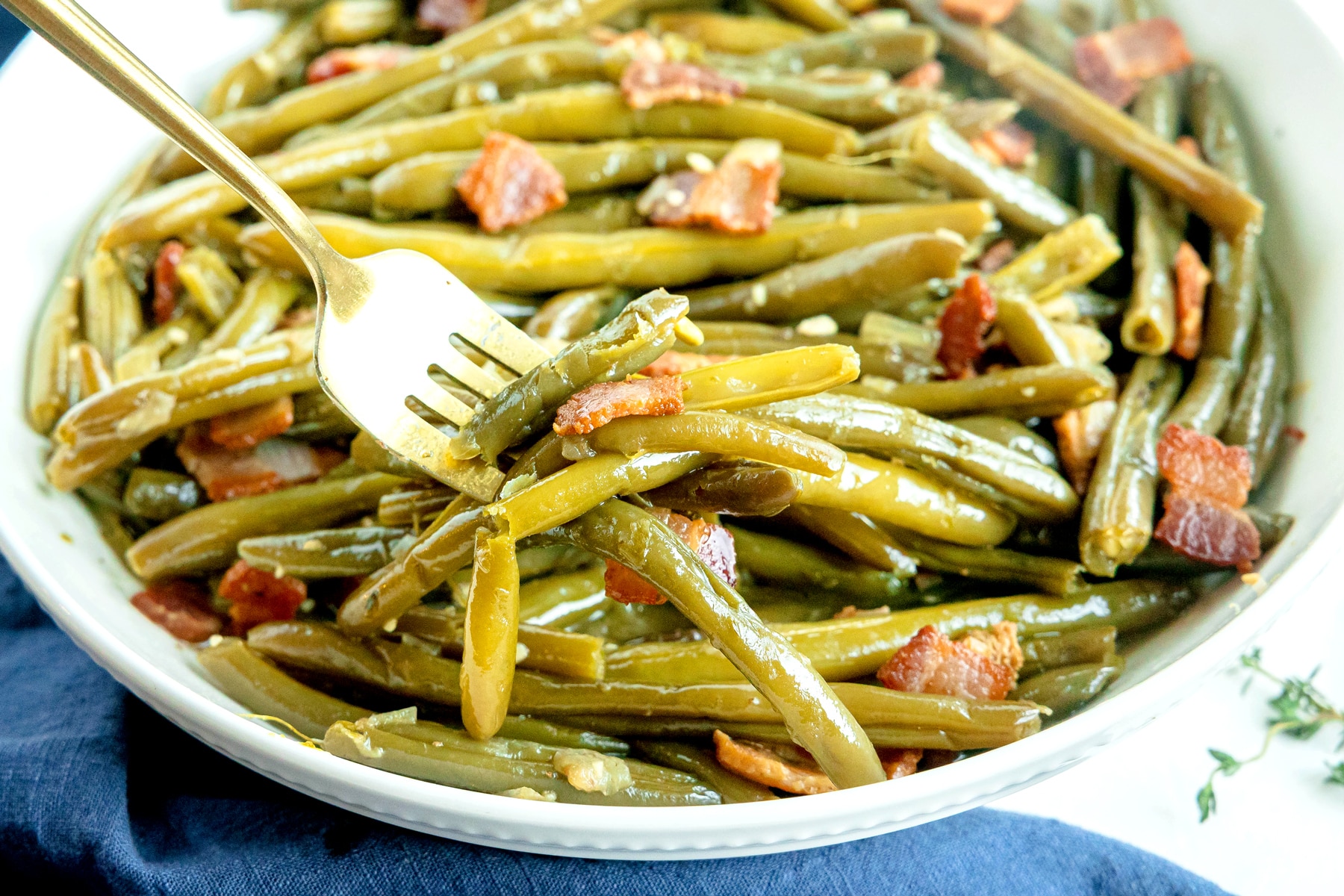 A serving of Southern Green Beans with a fork lifting green beans and bacon pieces.