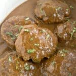 Crockpot Salisbury steak patties smothered in brown gravy and garnished with chopped parsley.