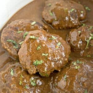 Crockpot Salisbury steak patties smothered in brown gravy and garnished with chopped parsley.